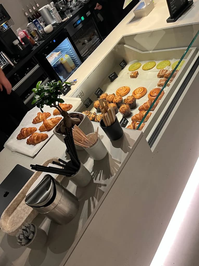 Tresenansicht mit täglich frischen Pastries, Croissants, Pain au Chocolat, Muffins, Cookies und grüne Matcha-Cookies in der Vitrine, daneben ein Bonsai im Steingefäß.