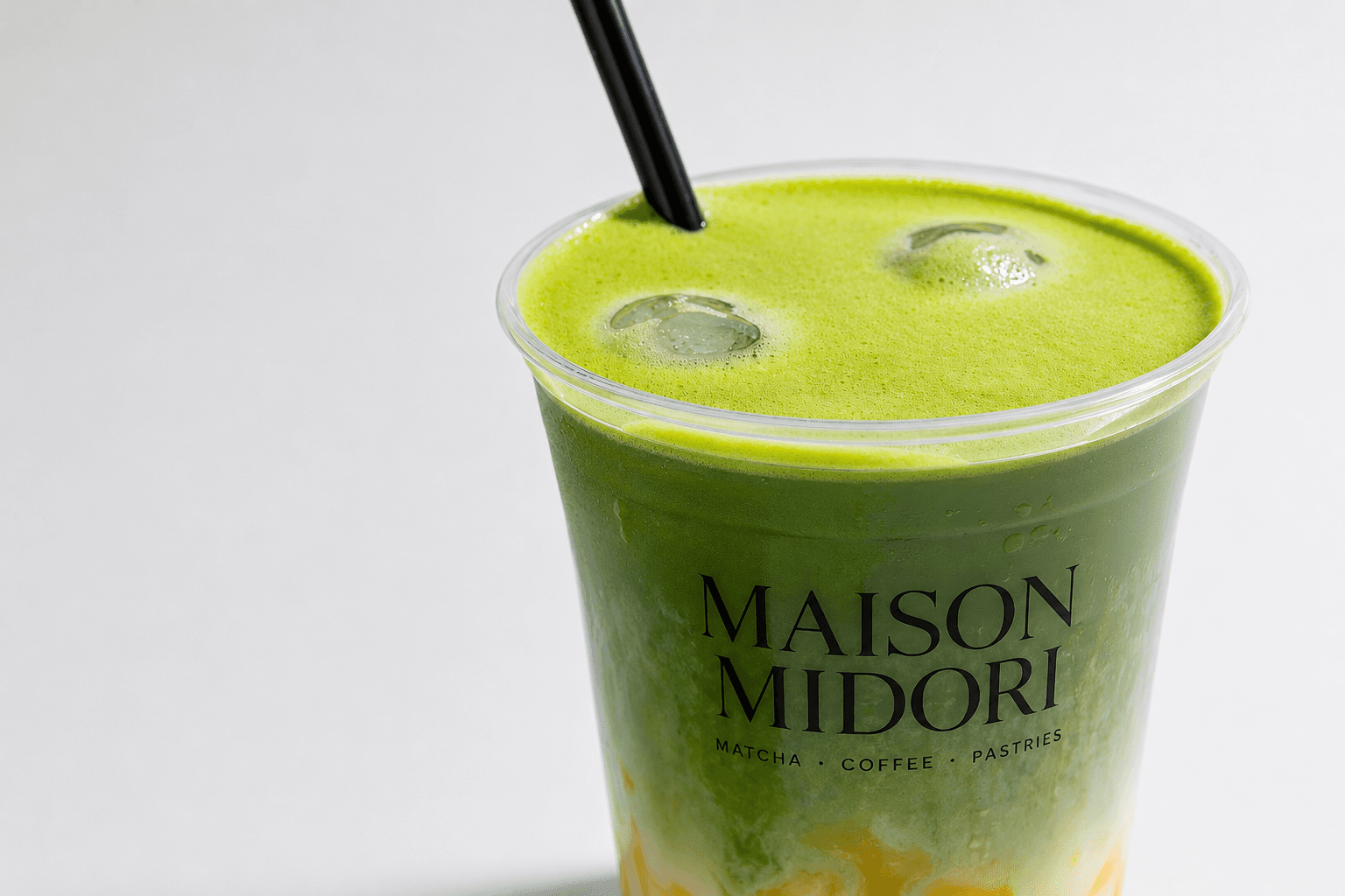 Nahaufnahme von oben auf einen frisch gegossenen Iced Matcha im Maison-Midori-Becher mit schwarzem Strohhalm